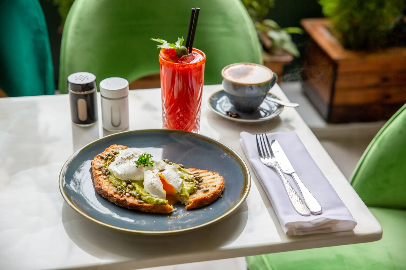 Savor a delightful breakfast featuring avocado toast, poached eggs, cappuccino, and a refreshing drink indoors.