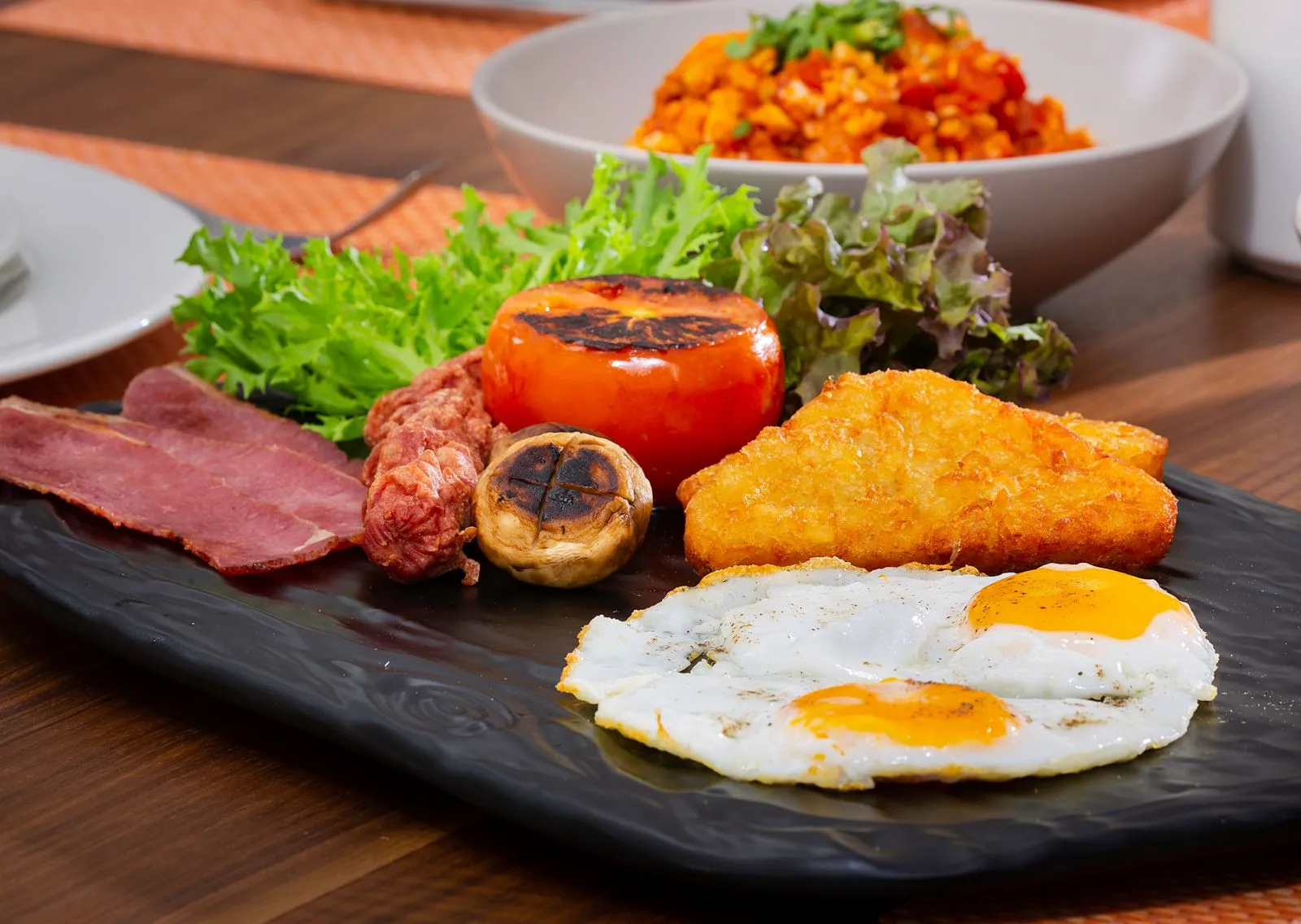 Close-up of a breakfast platter with fried eggs, bacon, and vegetables.